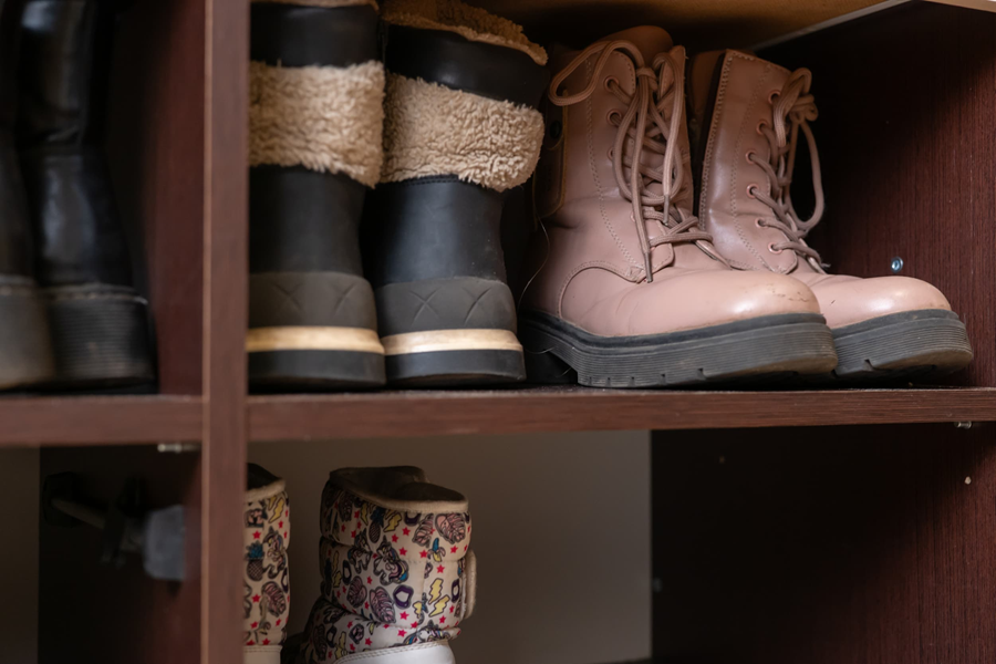 Several pairs of winter boots are stored neatly on a wooden shelf indoors.